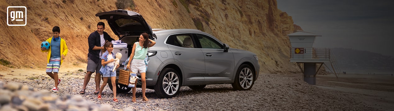 Family at a Beach With Their Buick Avenir SUV in the Background with an Overlay of GM Logo
