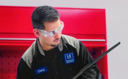 A Technician Named Chris in a General Motors Certified Service Uniform and Safety Glasses Holding a Car Part