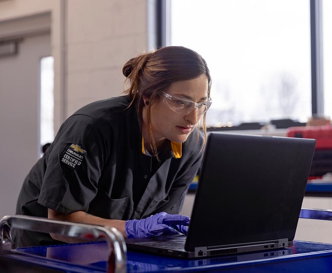 A Woman in a General Motors Certified Service Uniform and Safety Glasses Using a Laptop