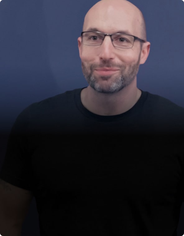 A Man with Glasses and a Beard Smiling Against a Blue Background