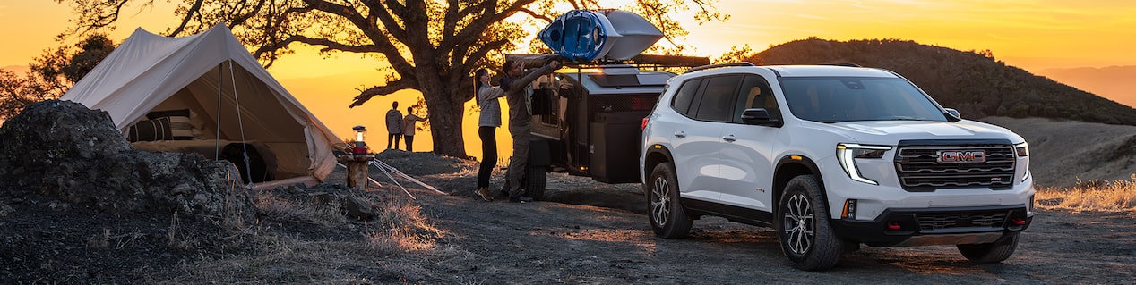 Three Quarters View of a White GMC SUV in Front of a Trailer with the Sunset Behind