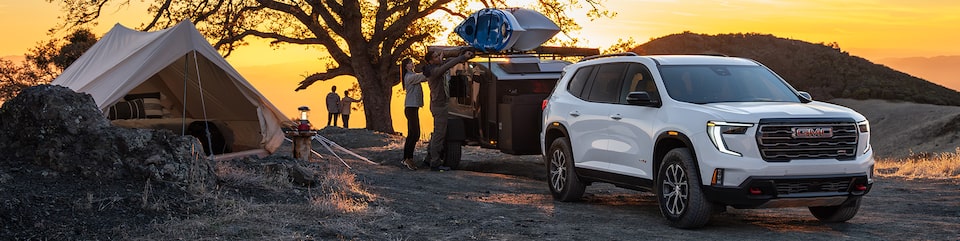 Three Quarters View of a White GMC SUV in Front of a Trailer with the Sunset Behind