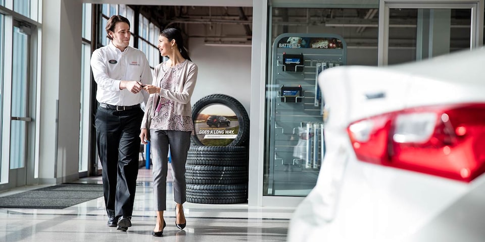 Man & Women In Dealership Exchanging Keys