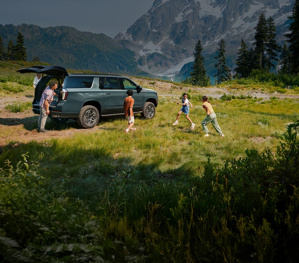 GM vehicle parked in field with kids playing with mountain backdrop