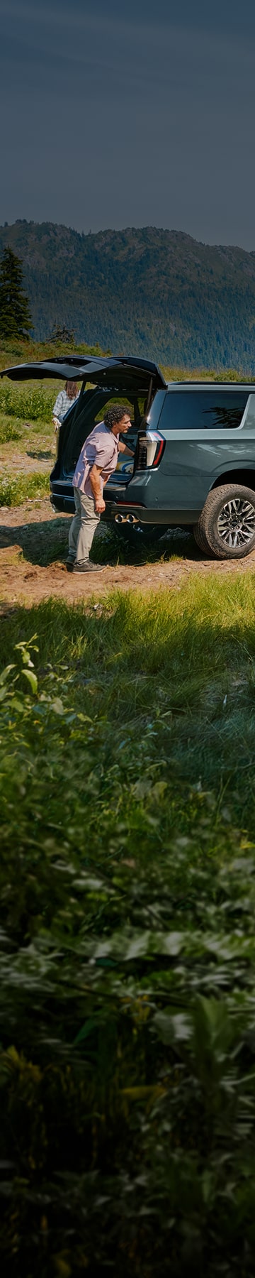 GM vehicle parked in field with kids playing with mountain backdrop 