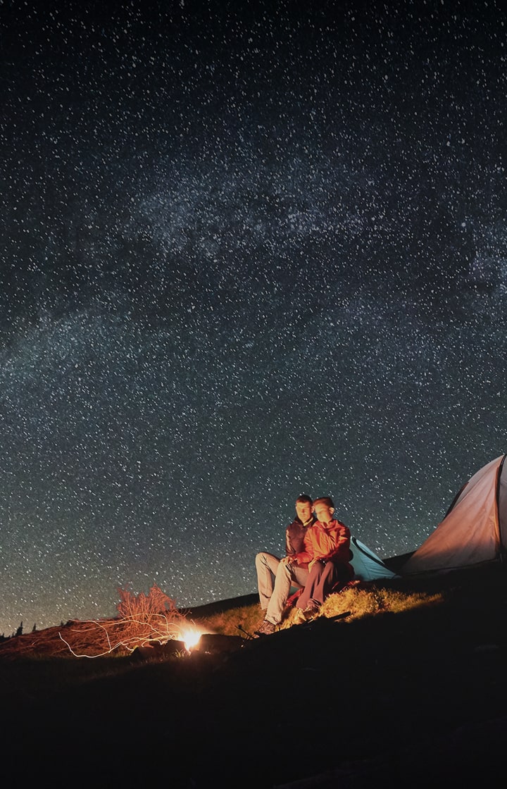 Man and woman camping and sitting around a fire under a starry sky
