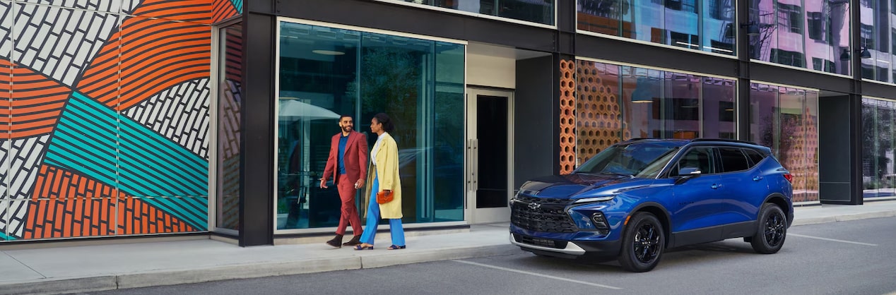 Couple holding hands while walking down a colorful city street and passing a GM vehicle