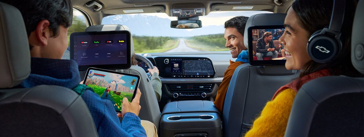 A family seated in a vehicle with the dad in the front passenger seat looking back at his kids.