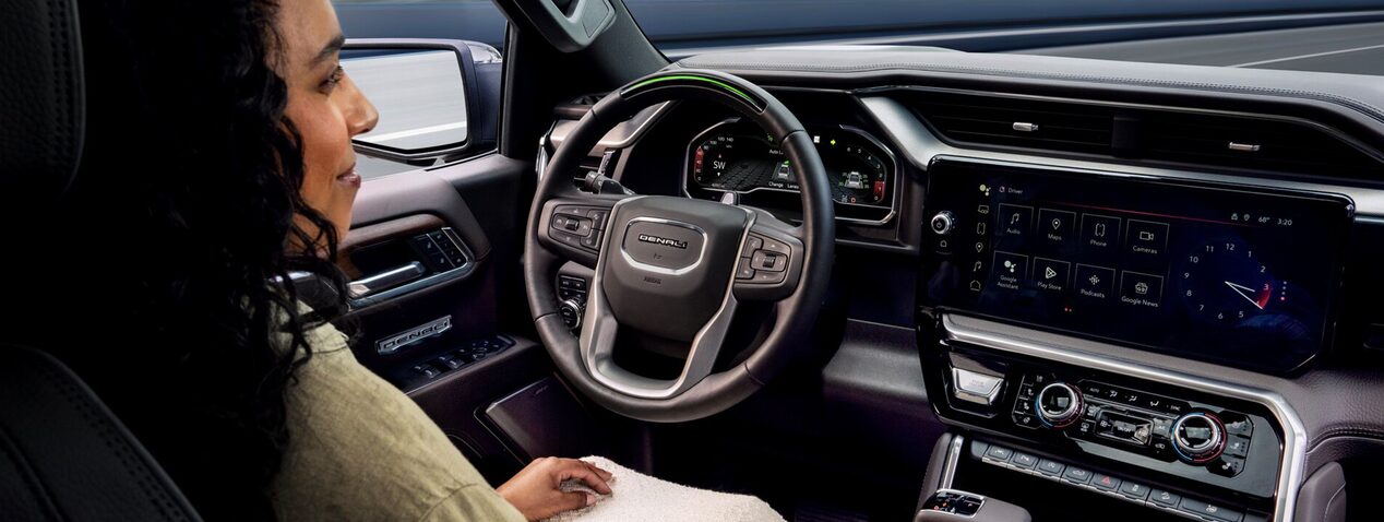 A woman seated in the driver's seat of a vehicle with her left arm resting on the window.