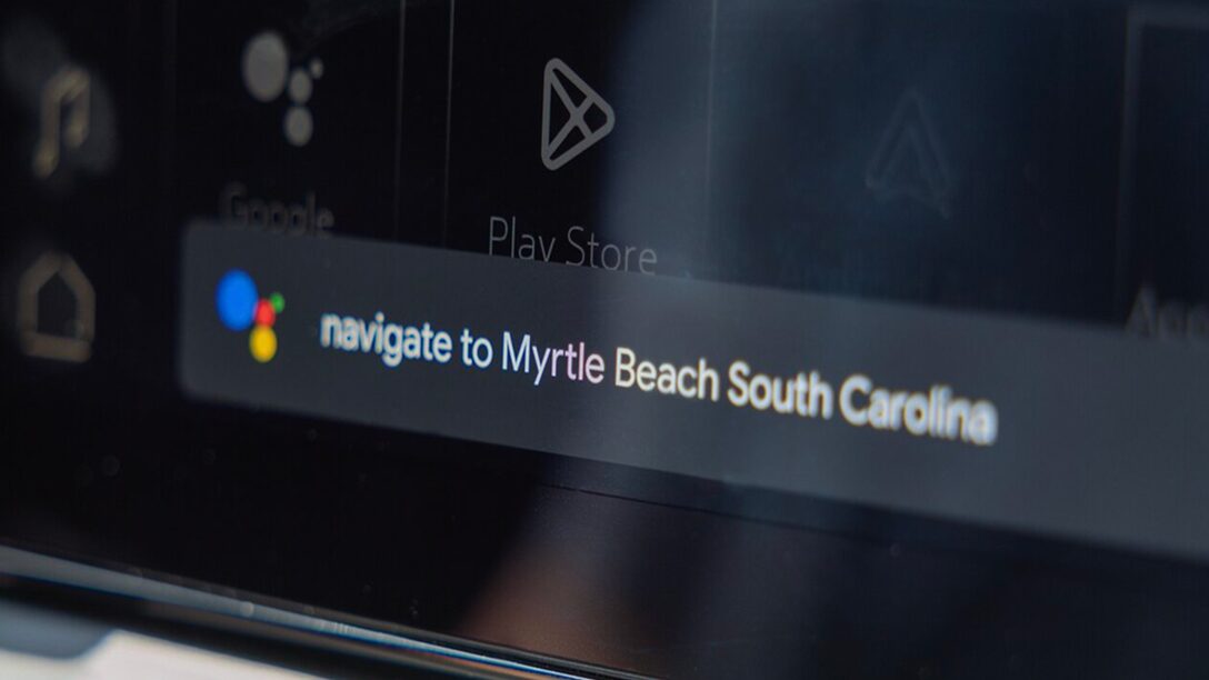 A vehicle's digital display shows the Google Assistant voice command interface with the text 'navigate to Myrtle Beach South Carolina' displayed in the search bar.
