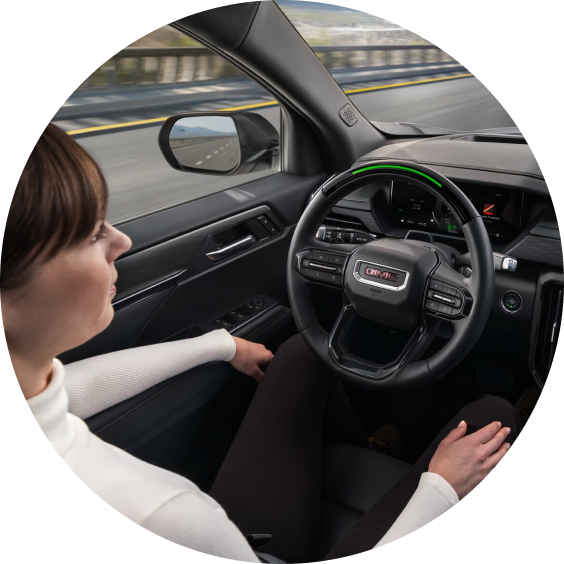 A woman is driving a vehicle with the GMC logo on the steering wheel