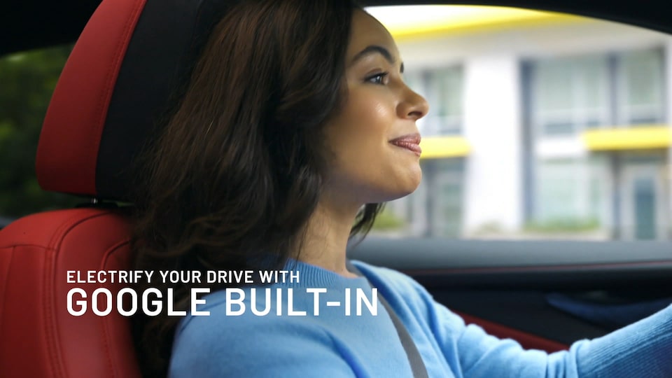 A woman driving a car with text overlay "Electrify your drive with Google Built-In"