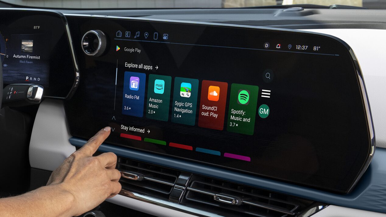 A hand touches the vehicle's infotainment screen, which displays a grid of Android Apps icons including Waze, Google Maps, YouTube Music, and Spotify.