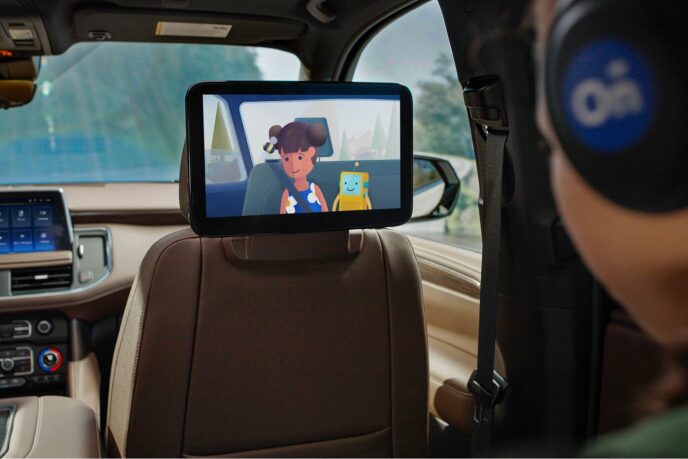 A kid is wearing headphones in the passenger seat while watching cartoons on the display attached to the front seat of the vehicle.