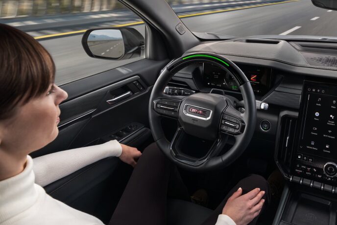 Overhead view of a woman in the driver’s seat in a self-driving GMC vehicle not holding the steering wheel on the road.