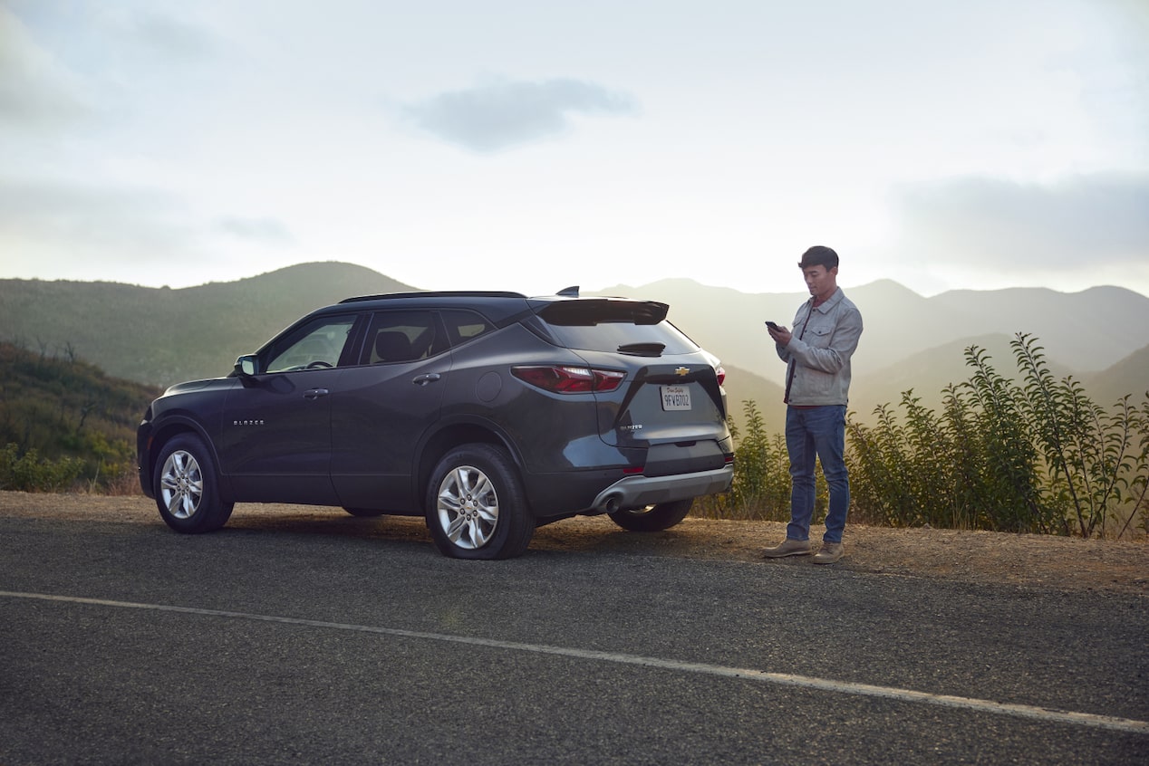 Man Standing Next to Vehicle on the Side of the Road Using his Smartphone