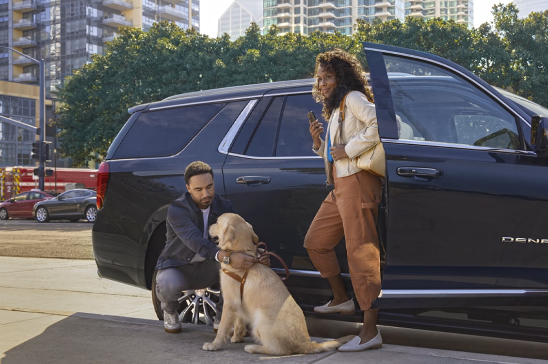 Side view of a black SUV with a woman getting out of it and a man petting a dog next to It