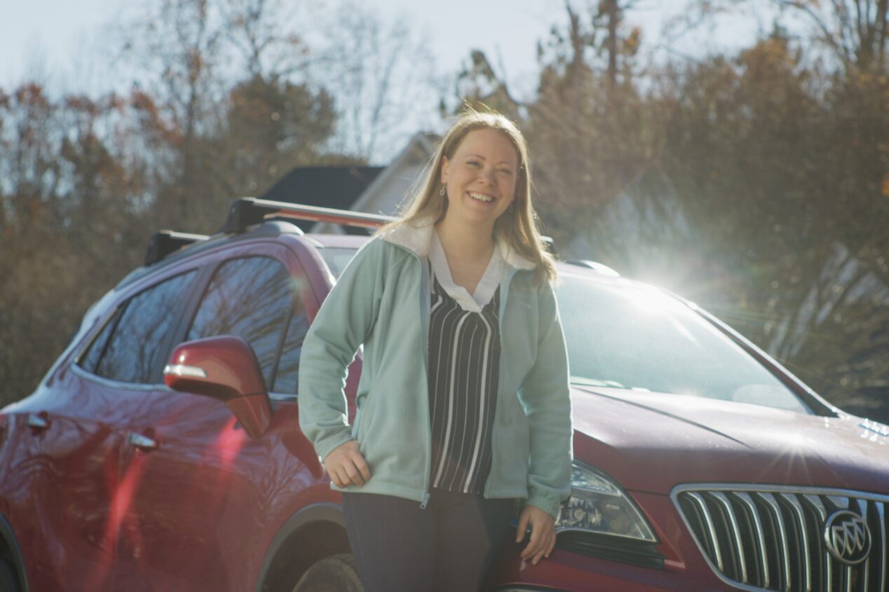 Woman Smiling and Leaning on the Hood of her Vehicle