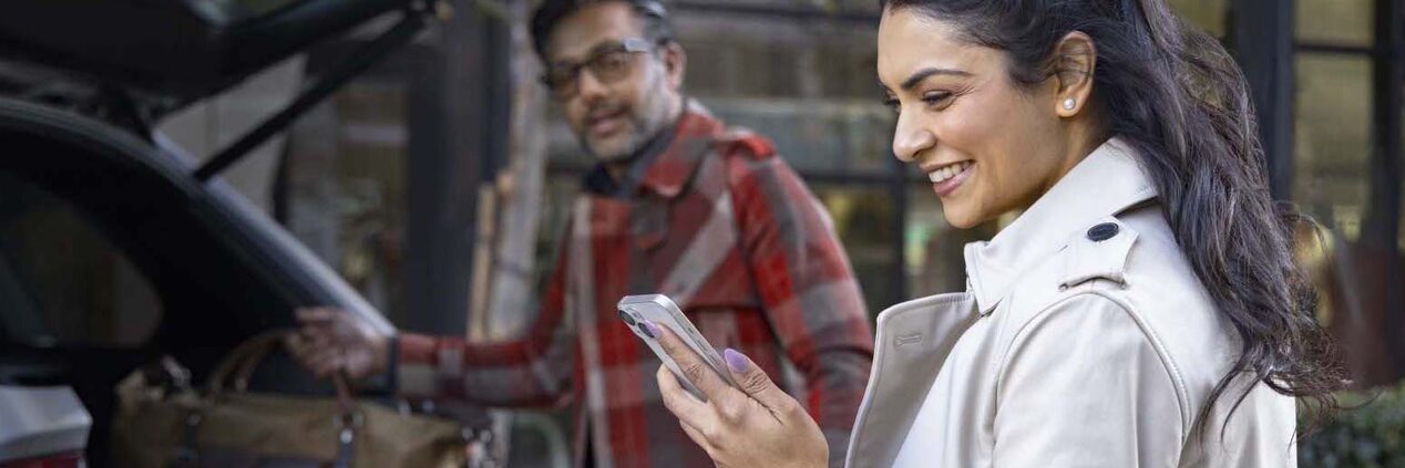 Man Loading Luggage into Vehicle While Women Smiles at Smartphone