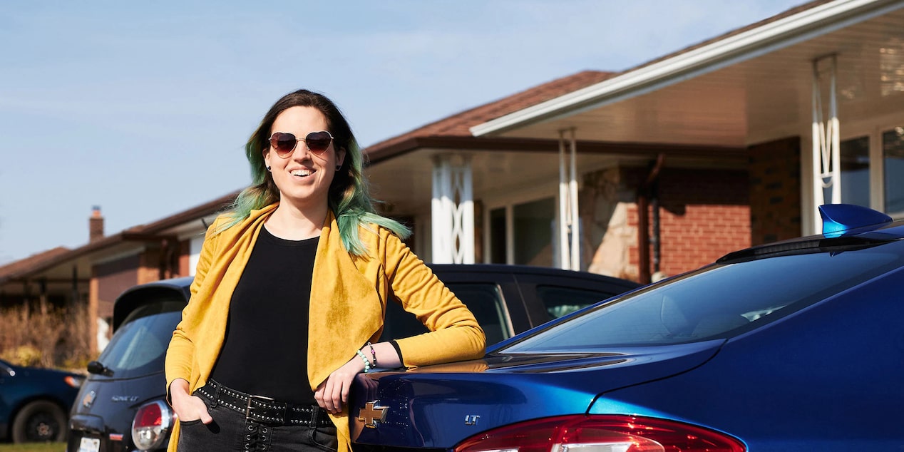 Woman Standing Smiling on the Rear of her GM Car