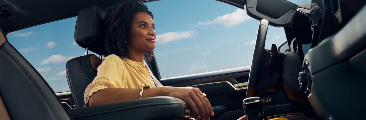 A woman sitting in the driver's seat of a vehicle with her right arm resting on the center console.
