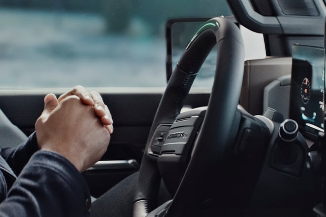 Close-up of a driver's hands clasped together in front of the steering wheel, while they use Super Cruise driving technology