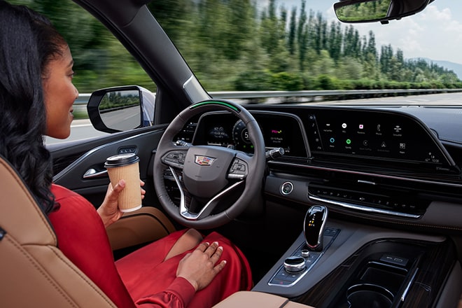 A woman drives using Super Cruise hands-free driving technology while holding her coffee and resting her other hand on her lap